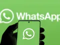 Hand hält Smartphone mit WhatsApp-Logo vor grünem Hintergrund.