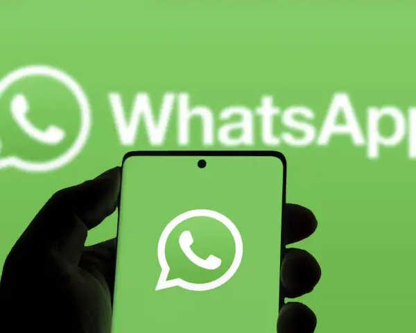 Hand hält Smartphone mit WhatsApp-Logo vor grünem Hintergrund.