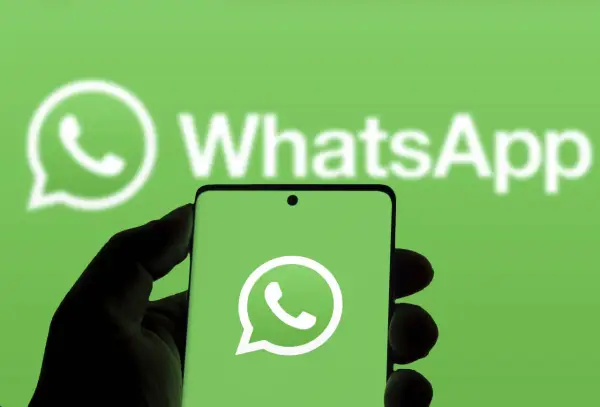 Hand hält Smartphone mit WhatsApp-Logo vor grünem Hintergrund.